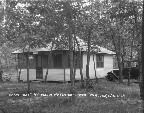 Exterior view of one of the larger guest cabins with screened-in porch at Clearwater Cottages. An automobile is parked on the right.