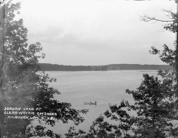 View from hill of Jordan Lake. Two people are fishing in a rowboat below, and the wooded far shoreline is in the distance.