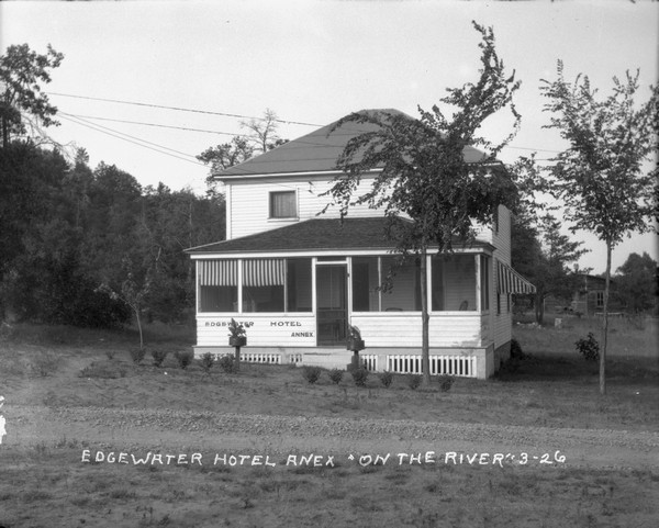 Exterior view of the Edgewater Hotel Anex [sic] which has a screened-in porch. Young trees are planted in the lawn.