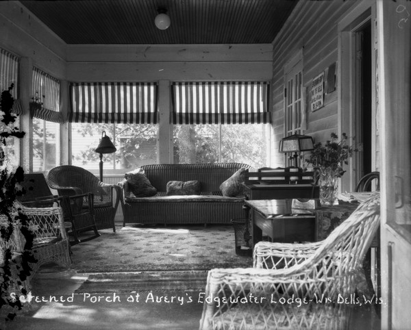 Screened porch furnished with wicker chairs and a sofa, lamps and a rug.
