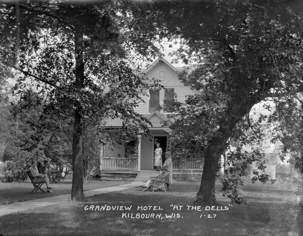 View of the main building at the Grandview Hotel. There are women posed on the porch and on the lawn near the front walk.