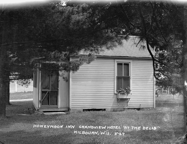 Exterior view of a small cottage at the Grandview Hotel. Flowers are in a window box and an automobile is parked in back.