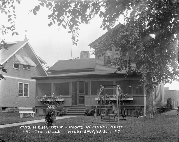 Exterior view of a house in a residential neighborhood with a large screened-in porch, and a bench and a lawn swing in the front yard.