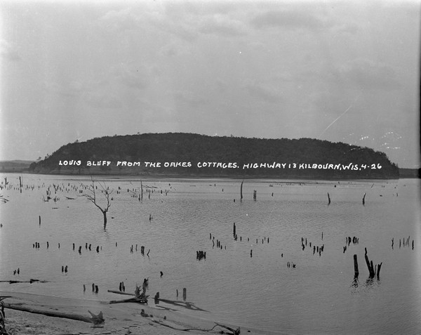 View from shoreline, with tree stumps sticking above the waterline, of the Wisconsin River and Louis Bluff from Oakes Cottages.