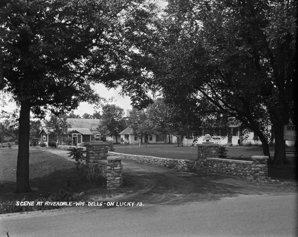 View from road of the entry drive with stone walls on each side, leading to the Riverdale Resort. The main building is on the right across the lawn.