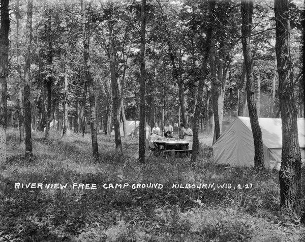 The campsites among the trees and tall grass at Riverview Campground. A few tents are set up, and a group of guests are around a picnic table.