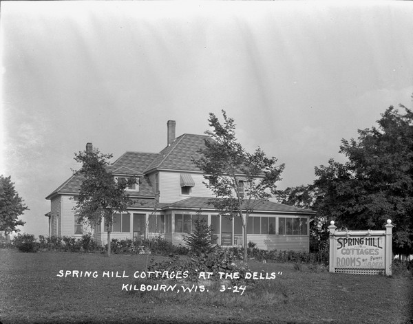 The main building at Springhill Cottages, with a screened-in porch and a large billboard in front advertising cottages and rooms with private baths.