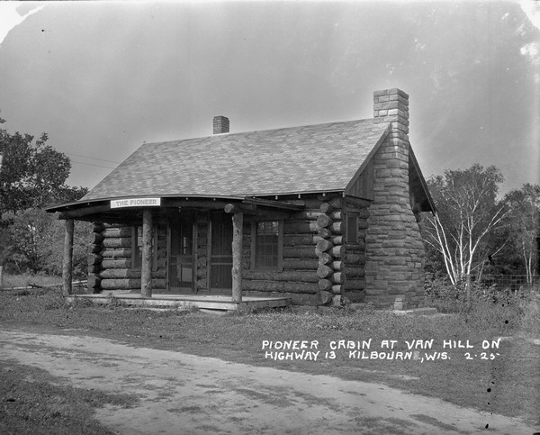 The "Pioneer Cabin" at Van Hill Cabins, with two entrances and log columns on the porch. A stone chimney is on the right.