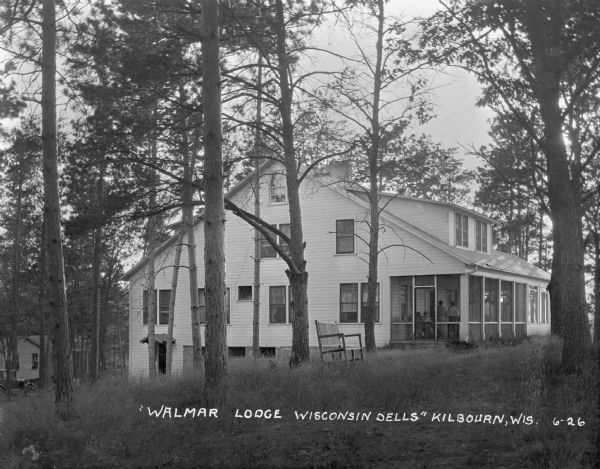 Screened-in porch side of Walmar Lodge. A bench is under the trees, and an automobile is parked on the left.