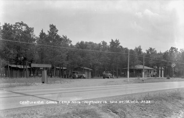 View from other side of road towards the Continental Cabin Camp and Texaco station along Highway 12. There are people standing near two parked cars.