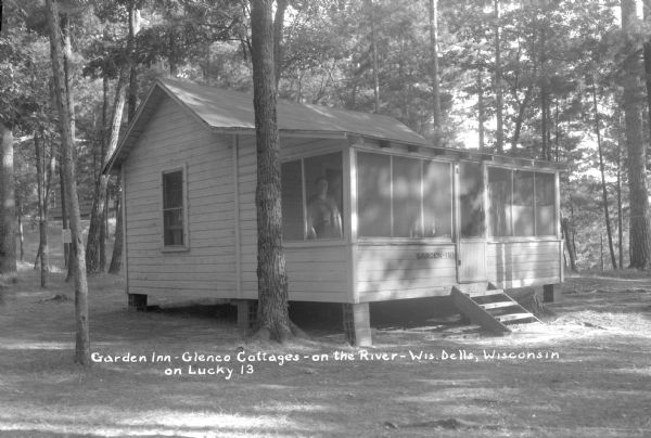 One of the guest cottages at Glenco Cottages. The cottage is raised above the ground on concrete blocks. A woman is standing in the screened porch.