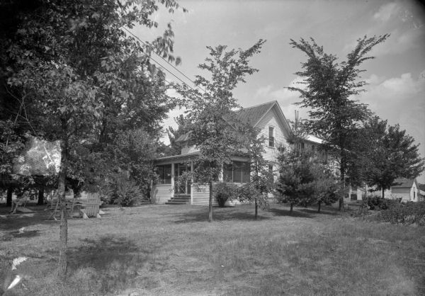 Side view across lawn of the Grand View Hotel, with a porch in the front. Cottages are in the background on the right. Women are sitting in the lawn chairs on the left.