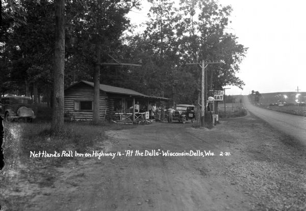 View from side of road towards main building of Nettland's Roll Inn, with a service station, restaurant and registration office for their campsites. A group of people are posed next to an automobile parked near the porch. Another automobile is parked behind the building on the left.