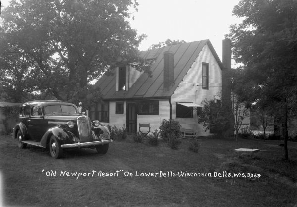 Riverside cottage with an automobile parked in front. The license plate reads: "Wisconsin 1938."