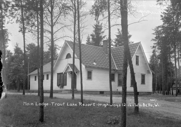 Exterior view through trees of the main lodge at Trout Lake Resort. A driveway is in front of the entrance which has a half-circular window above the door.