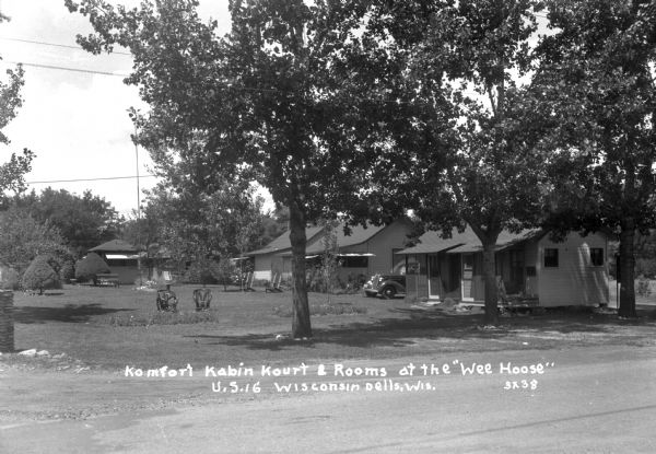 View from road of row of cabins with chairs on the lawn in front. There is an automobile parked behind the first cabin.