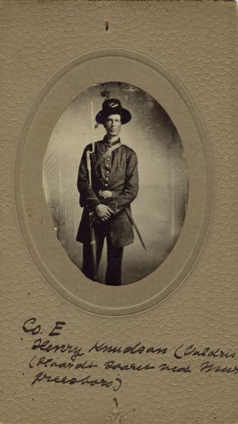Three-quarter length oval studio portrait of Henry Knudson, a private in Company E, 15th Wisconsin Infantry, in uniform, cradling his musket with a bayonet attached. The following information was obtained from the Regimental and Descriptive Rolls, Volume 20: He resided in Moscow, Wisconsin. On December 2, 1861, he enlisted in Iowa County, Wisconsin and was mustered into service in Madison, Wisconsin on December 08, 1861, at the age of 19. He was discharged on November 24, 1862, at Edgefield, Tennessee for re-enlistment into the 4th U.S. Cavalry.
