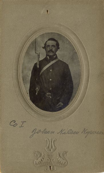 Waist-up oval portrait of Johan Nilson Nysveen [as written on the photograph backing; also written as John Nilson on Descriptive Rolls, Volume 20 and published rosters: Rosters of Wisconsin Volunteers, Volume 1 (1886) and Wisconsin Volunteers: War of the Rebellion (1914)], a private in Company I, 15th Wisconsin Infantry. The following information was obtained from the Regimental and Descriptive Rolls, Volume 20: He resided in Waupaca, Wisconsin. On October 30, 1861, he enlisted in Scandinavia, Wisconsin and December 20, 1861, he was mustered into service in Madison, Wisconsin at the age of 27. On August 27, 1863, he was absent on furlough in Waupaca County, Wisconsin. As of June 08, 1863, he was listed on the muster rolls as being absent in Eau Claire, Wisconsin without leave. On May 23, 1864, he was detached to serve in the Brigade Provost Guard. From June through August 1864, he served at the Brigade headquarters. He was mustered out of service with Company I on February 10, 1865 at Chattanooga, Tennessee.
