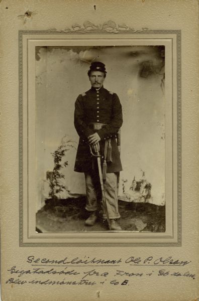 Full-length studio portrait of Ole P. Olson, a second lieutenant in Company B, 15th Wisconsin Infantry, in uniform holding a sword. The following information was obtained from the Regimental and Descriptive Rolls, Volume 20: He resided in Coon Prairie, Wisconsin. On September 23, 1861, he enlisted as a sergeant and mustered into service, in Madison, Wisconsin at age 22. On November 1, 1863, he was promoted to second lieutenant. He resigned his commission on June 6, 1863, due to disability.