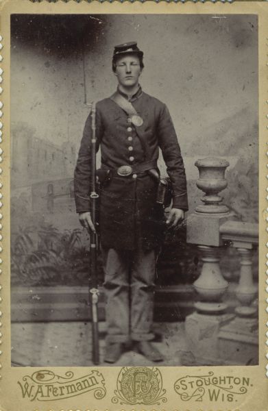 Full-length cabinet card portrait in front of a painted backdrop of Torger Larson, a private in Company H, 15th Wisconsin Infantry in uniform holding a musket next to a prop baluster and railing. The following information was obtained from the Regimental and descriptive Rolls, Volume 20: He resided in Deerfield, Wisconsin. On February 9, 1864, he was enlisted into service in Madison and on February 16, 1864, he was mustered into service at the age of 19. On March 31, 1964, he joined Company H as a recruit at Strawberry Plaines, Tennessee. On May 27, 1864, he was wounded during the battle at New Hope Church, Georgia. On June 10, 1865, he was transferred to Company I, 13th Wisconsin Infantry. He was mustered out of service on May 10, 1865, in Davenport, Iowa by authority from the War Department, Army General Order dated May 3, 1865.
