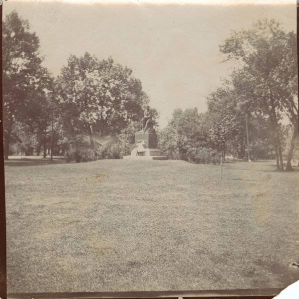 View across lawn of a two children standing at the base of a statue on a pedestal.