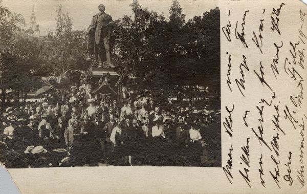 Elevated view of a crowd of people surrounding a statue, presumably of a notable Norwegian figure. Many people are carrying flags.