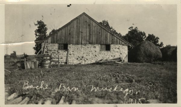 Exterior view of the Bache barn with stone foundation. There are large haystacks on the right.