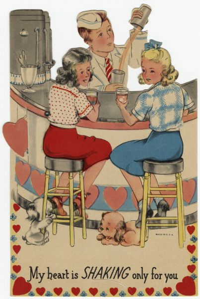 Valentine's Day card of a soda fountain with two girls seated on stools in front of the counter and a soda jerk behind. Two puppies are on the floor near the girl's stools. Coffee urns are on the counter. The soda jerk is hinged with a metal eyelet so he appears to be "shaking" an ice cream treat. The girls are wearing blouses, skirts, bobby socks and shoes. The soda jerk is wearing a a uniform. Hearts and flowers decorate the counter and the bottom of the card. Offset lithography and die cut.