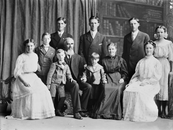 Studio portrait in front of a painted backdrop of eleven members of the Nyhus family, including four women, four men, and three young boys.