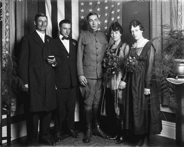 The bride, groom, wedding party, and pastor(?) pose for the Stafford-Harold wedding portrait. The groom wears a military uniform from the World War I era.