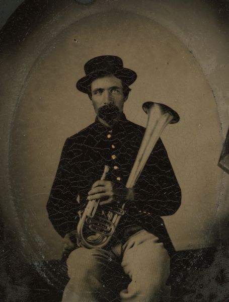 Tintype portrait of Thomas H. Brown of Shullsburg, Wisconsin, member of the 3rd Wisconsin Infantry band.  He is seated in uniform and holds an alto horn. The buttons on his uniform are hand-colored gold.