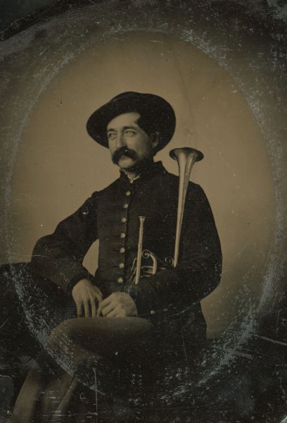 Tintype portrait of William G. Douglas of Shullsburg, Wisconsin, member of the 3rd Wisconsin Infantry band. He is seated in uniform and holds an E-flat horn. The buttons on his uniform are hand-colored gold.