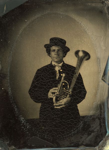 Tintype portrait of F.A. Knickerbocker of Shullsburg, Wisconsin, member of the 3rd Wisconsin Infantry band. He is standing in uniform and is holding an alto horn. The buttons on his uniform are hand-colored gold.