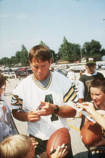 Green Bay Packer quarterback Brett Favre signing autographs for kids in the parking lot of Lambeau Field, near the Packer practice field. This photograph was taken by the Wisconsin Division of Tourism.