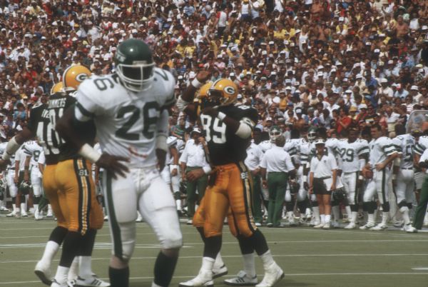 Packers players, with the jersey numbers 40 (Eddie Lee Ivery), 81 (Dan Ross) and 89 (Mark Lewis), high five each other after a play during a game against the New York Jets. The game was preseason and took place at Camp Randall Stadium. This was the largest crowd ever to see the Packers play in Wisconsin and the first pro football game ever held in Madison. The Packers won the game 38 to 14.