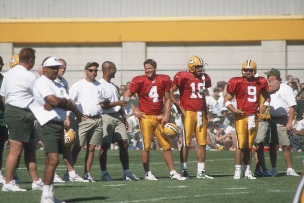 Brett Favre wearing a red jersey at Green Bay Packers training camp with other players and coaches.