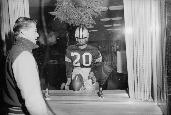 A teenage boy looks at a window display of a mannequin dressed up in a Packer uniform, as well as two small Packers bobble-head toys. The Packers were about to play for, and would go on to win, their seventh title as World Champions of Pro Football.