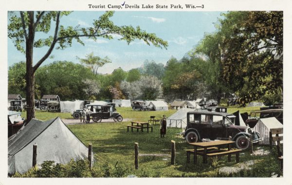 Colorized postcard of a tourist camp at Devil's Lake State Park. Features a scene of men, women and children among picnic tables, automobiles. Tents are pitched among trees, grass and shrubs. Caption reads: "Tourist Camp, Devil's Lake State Park, Wis.-3."