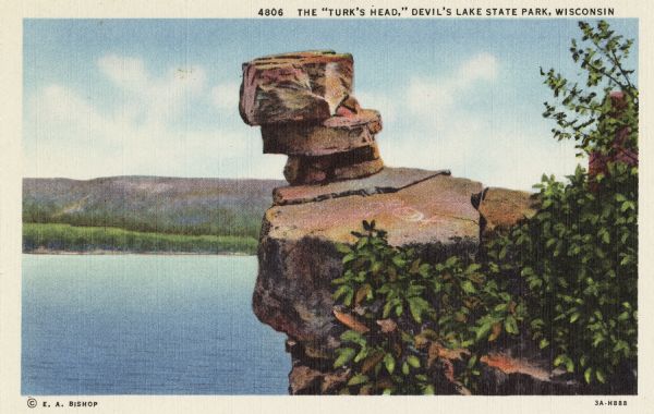 Colorized postcard of the rock formation called the Turk's Head in Devil's Lake State Park. Trees and foliage can be seen to the right and below. The lake, shoreline, bluffs and sky are visible in the background. The text above reads "Devil's Doorway, Devil's Lake State Park, Wisconsin."