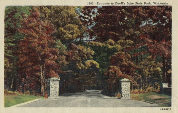 Colorized postcard of the entrance to Devil's Lake State Park. Trees and foliage fill the scene and it appears to be autumn. Stone pillars are on either side of the entrance. The text above reads: "Entrance to Devil's Lake State Park, Wisconsin."