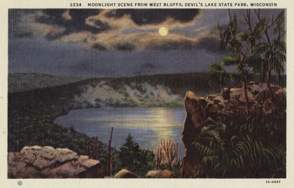 Colorized postcard of Devil's Lake by moonlight. Two rock formations and trees are in the foreground. The lake, trees, bluffs and sky are in the background. The text above reads: "Moonlight Scene From West Bluffs, Devil's Lake State Park, Wisconsin."