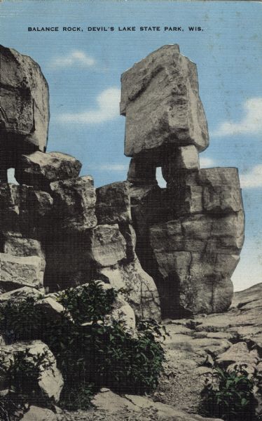 Colorized postcard of the rock formation called Balanced Rock in Devil's Lake State Park. Foliage can be seen below and the sky is visible in the background. The text above reads "Balance Rock, Devil's Lake State Park, Wis."