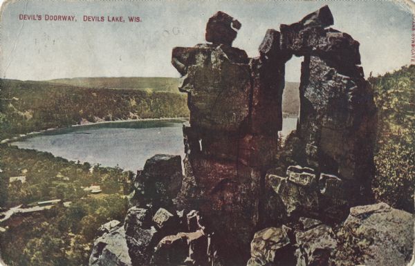 Colorized postcard of the rock formation called the Devil's Doorway in Devil's Lake State Park. The lake, bluffs, trees and sky are visible in the background. The text above reads "Devil's Doorway, Devil's Lake, Wis."