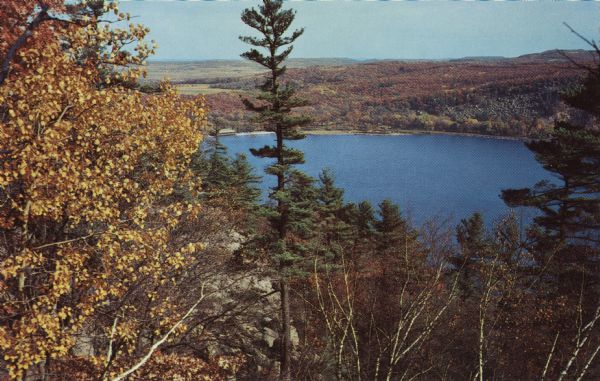 Color postcard of the lake viewed through the trees from the West Bluff in Devil's Lake State Park.