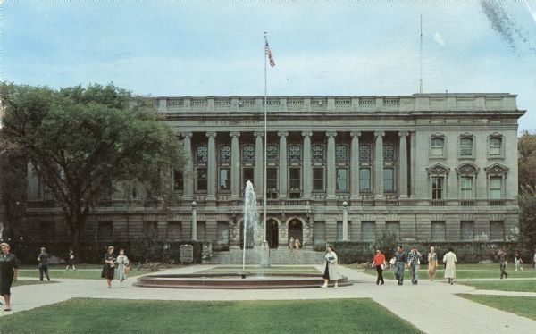 Color postcard of an exterior view of the Wisconsin State Historical Society Building, now the headquarters of the Wisconsin Historical Society. Students and patrons are  walking near the fountain in the middle of the Library Mall.