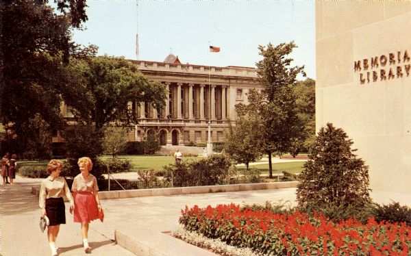 Color postcard of the exterior of the State Historical Society of Wisconsin from across the Library Mall. The University of Wisconsin Memorial Library is on the right. Two woman are walking towards the viewer.