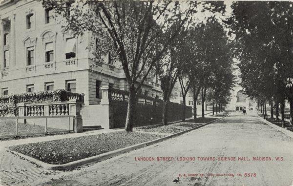 Black and white postcard of the north end of the State Historical Library, now the headquarters building of the Wisconsin Historical Society, and Langdon Street. Science Hall is visible at the end of the street. Many trees can be seen. The text below reads "Langdon Street, Looking Towards Science Hall, Madison, Wis."