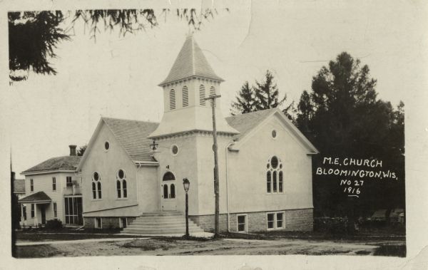 Photographic postcard of the Methodist Episcopal Church. Trees can be seen to the right and left. Text at the foot reads "M.E. Church, Bloomington, Wis., No. 27, 1916."