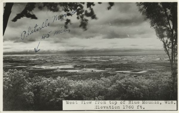 Photographic postcard of the view to the west from the top of Blue Mounds, in Blue Mounds State Park. Handwritten is "Platteville Mounds, 45 miles" with an arrow. Text below in a white box reads "West View from top of Blue Mounds, Wis. Elevation 1760 ft."