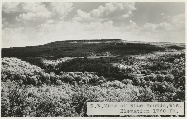 Photographic postcard of the northwest view of Blue Mounds. Text below in a white box reads "N.W. View of Blue Mounds, Wis. Elevation 1760 ft."
